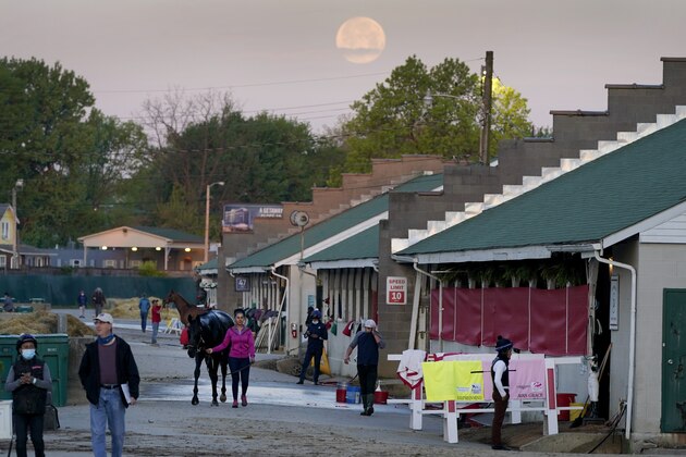 Workers tend to horses in barns as the full moon sets during morning workouts at Churchill Downs Tuesday, April 27, 2021, in Louisville, Ky. The 147th running of the Kentucky Derby is scheduled for Saturday, May 1. (AP Photo/Charlie Riedel)