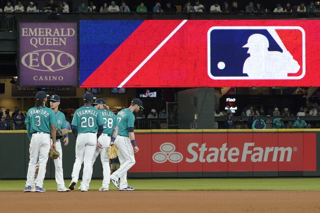 Seattle Mariners gather as the MLB logo is shown during a review of an attempted catch by right fielder Mitch Haniger of a ball hit by Tampa Bay Rays' Ji-Man Choi that was originally called an out during the ninth inning of a baseball game Friday, June 18, 2021, in Seattle. The call was overturned. The Mariners won 5-1. (AP Photo/Ted S. Warren)