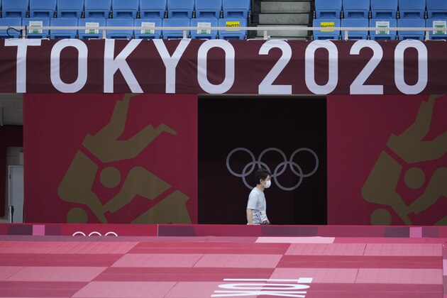 A worker walks under the Tokyo 2020 logo on the field of play for judo at the Nippon Budokan ahead of the 2020 Summer Olympics, Friday, July 23, 2021, in Tokyo, Japan. (AP Photo/Vincent Thian)