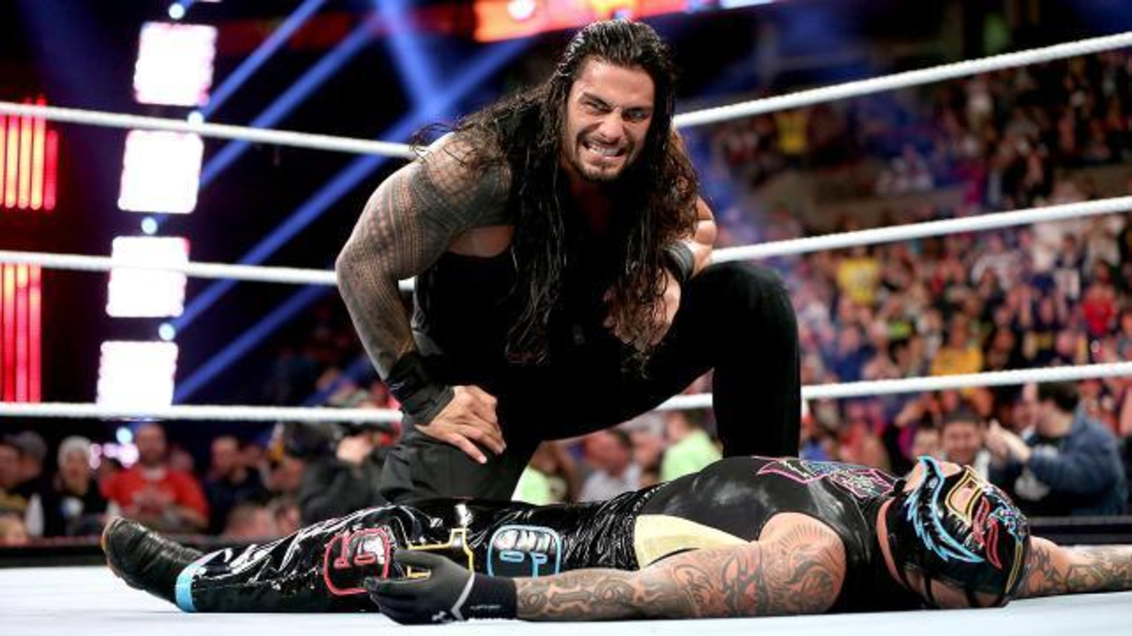 Roman Reigns kneels over his fallen prey, Rey Mysterio.