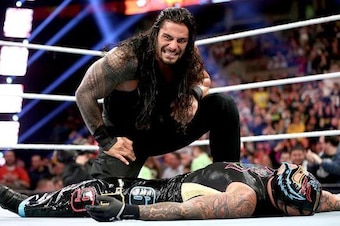 Roman Reigns kneels over the limp body of Rey Mysterio.