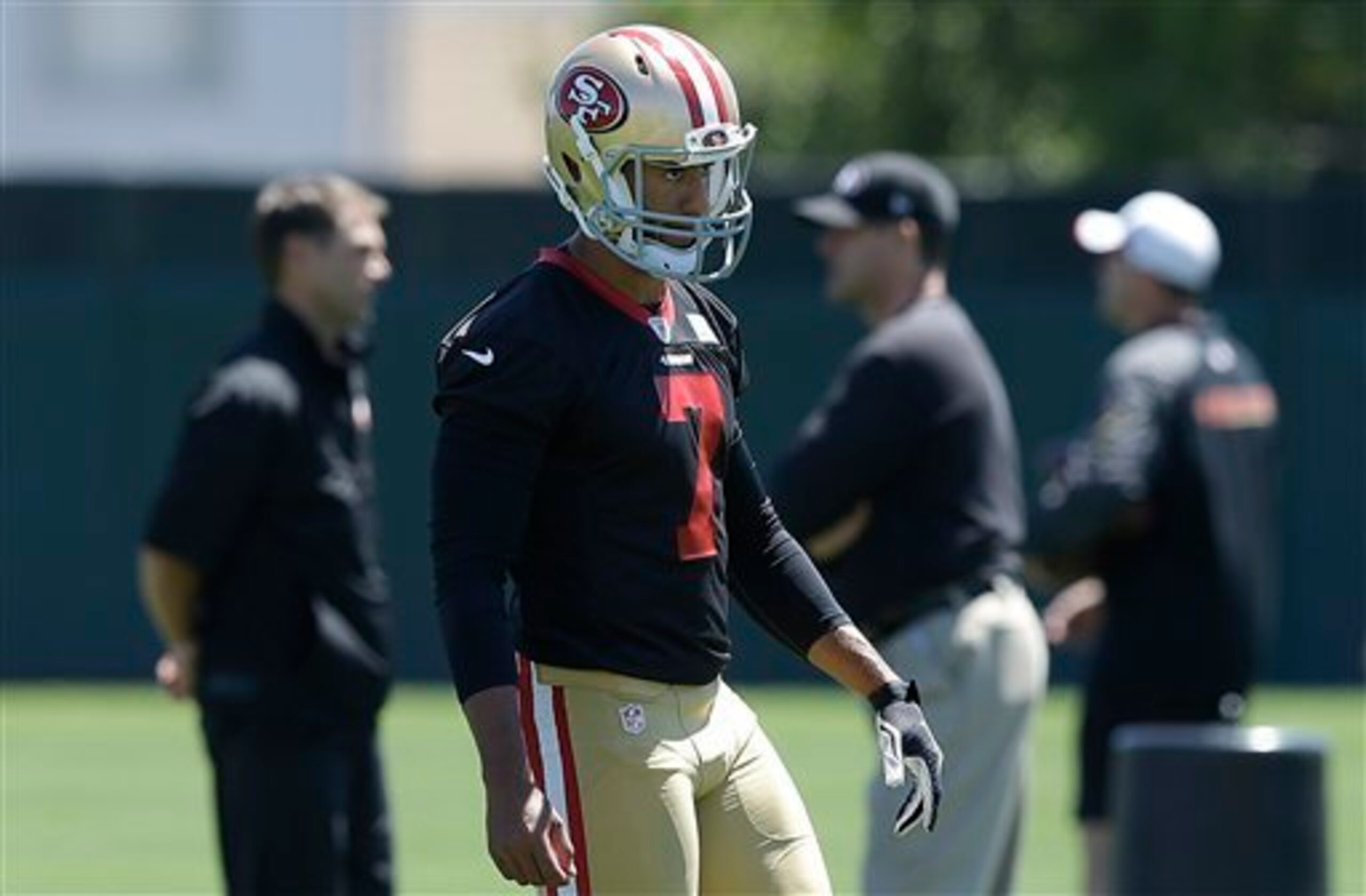 Kaepernick stays focused during an offseason camp while general manager Trent Baalke (left) and head coach Jim Harbaugh (right) discuss their all-world quarterback.