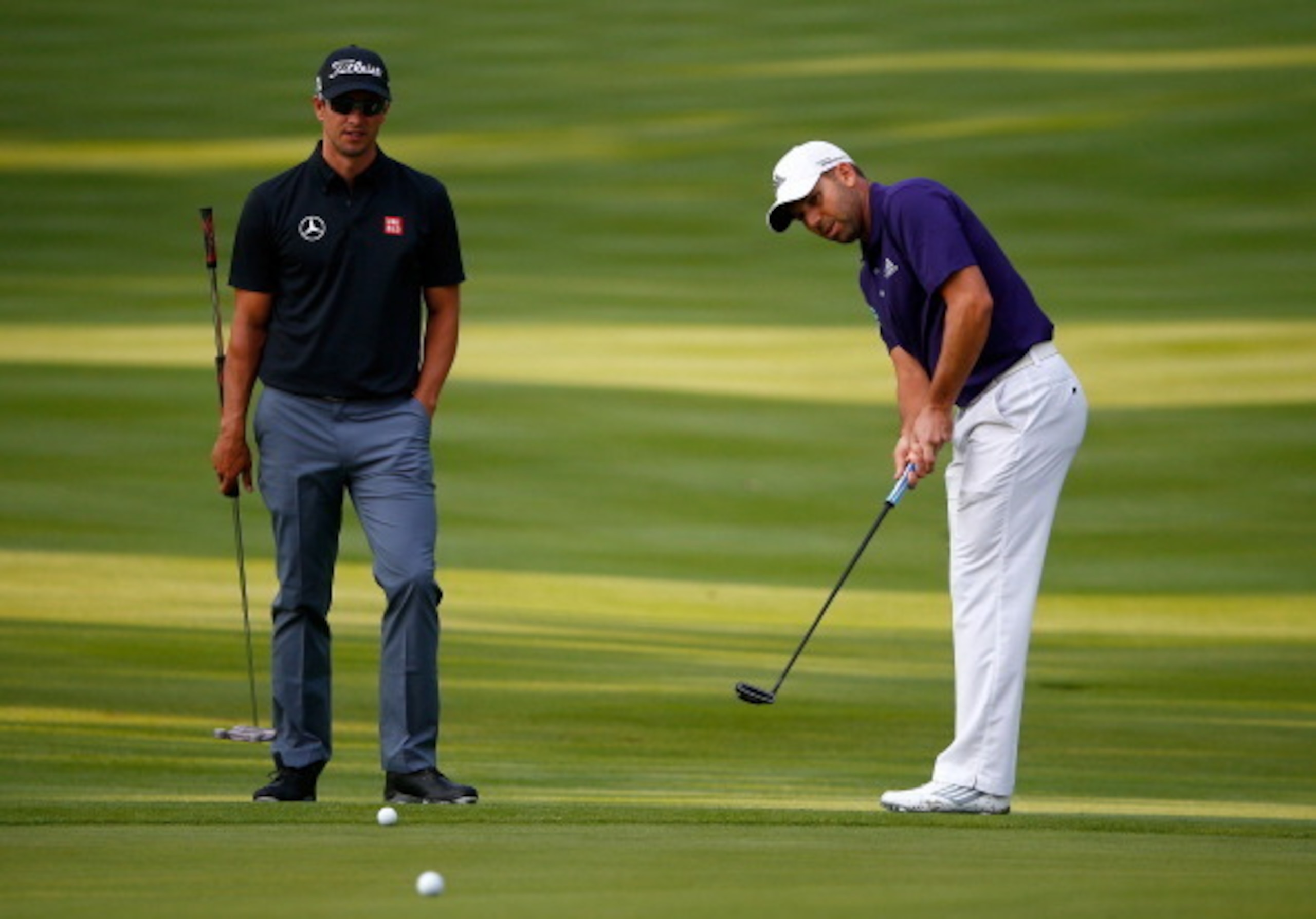 Sergio Garcia putts with Adam Scott looking on.