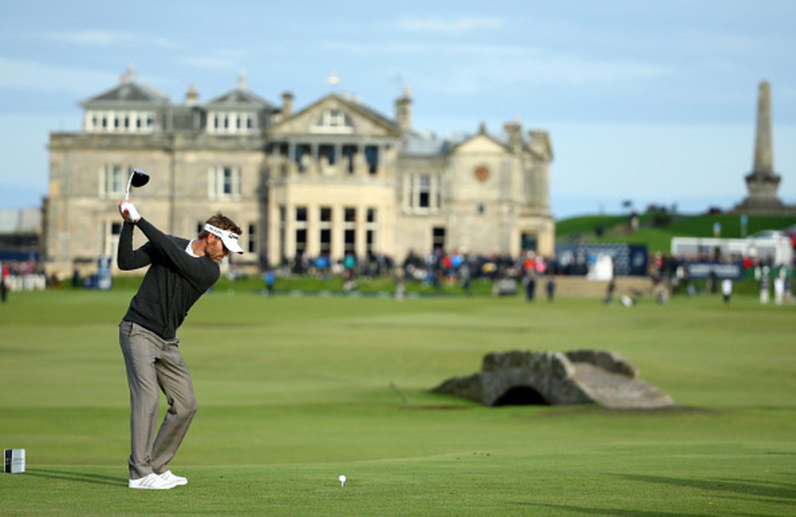 One of the most famous views in golf, teeing off on the 18th at St. Andrews, with the Swilcan Bridge in the foreground and the historic clubhouse in the background.
