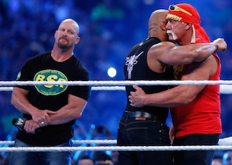 Steve Austin watches on as The Rock and Hulk Hogan embrace.