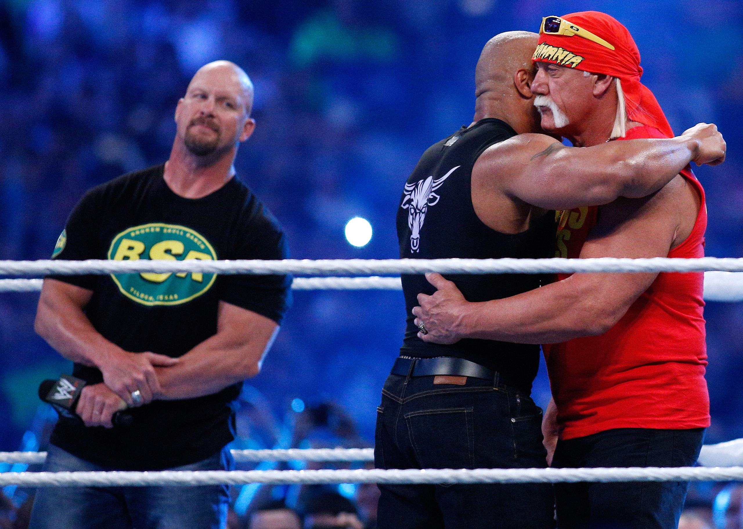 Steve Austin watches on as The Rock and Hulk Hogan embrace.