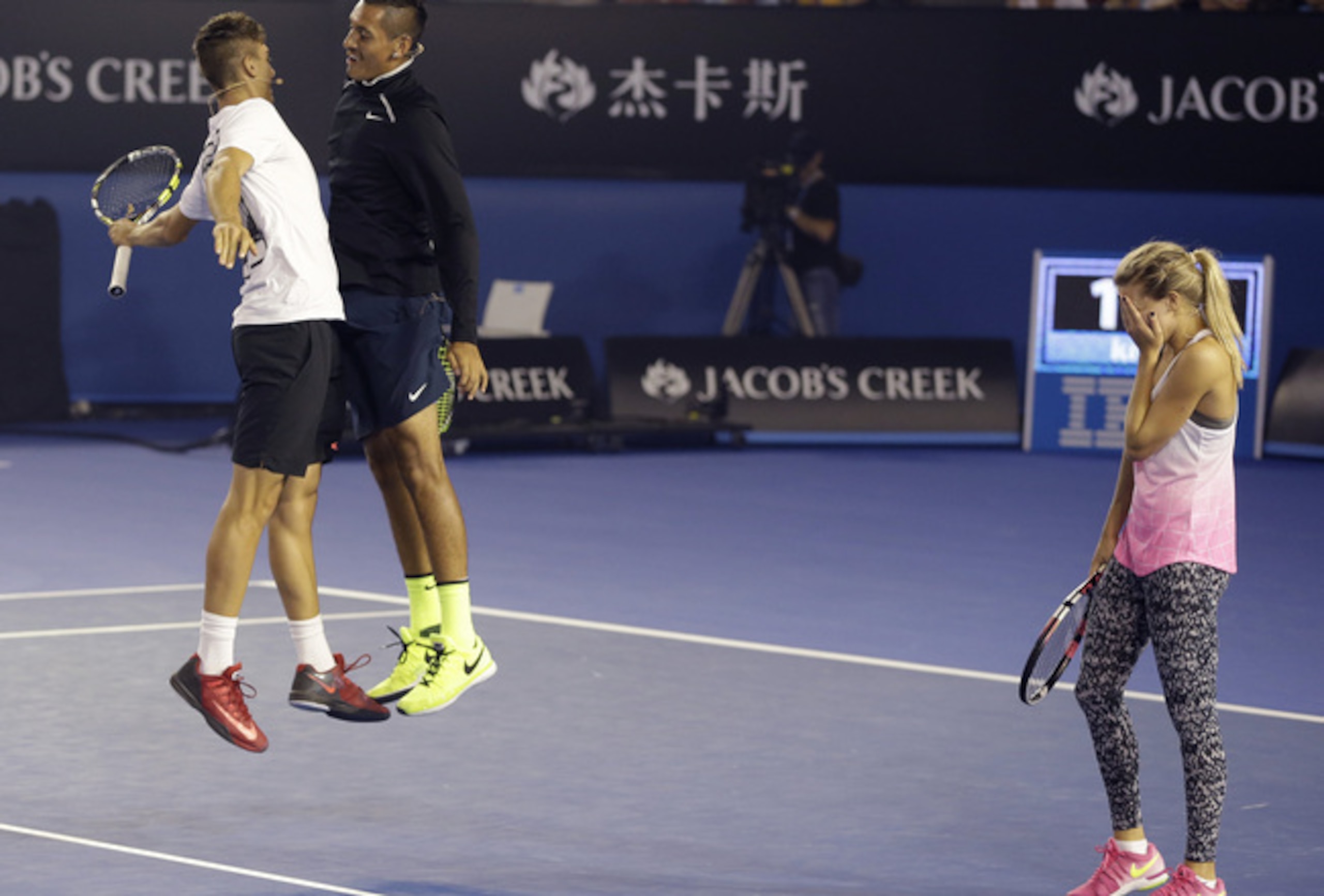 Nick Kyrgios and Thanasi Kokkinakis chest bump, while Eugenie Bouchard hides her face during an exhibition at the Australian Open.