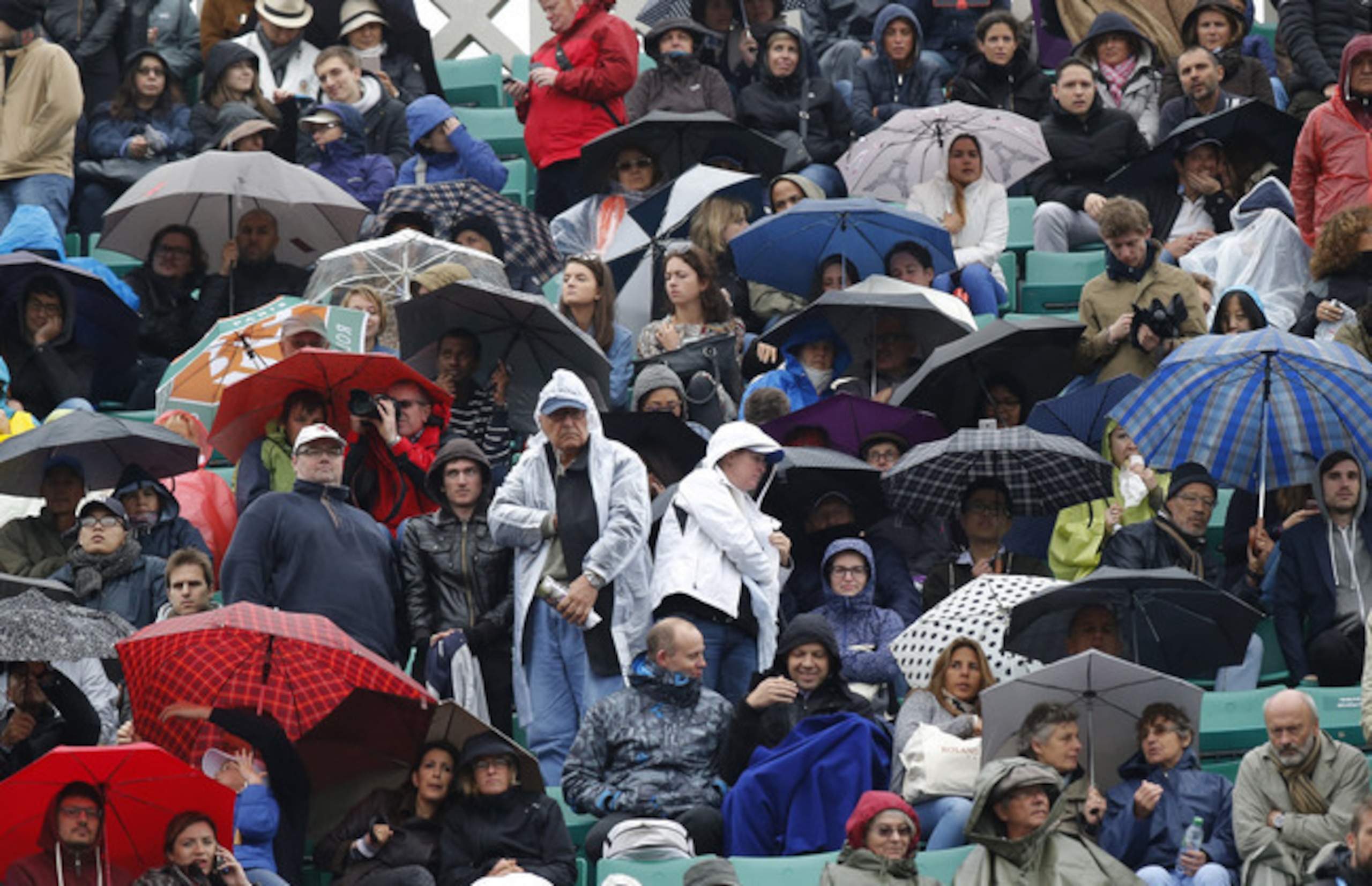 Fans cover up to endure rainy weather at Roland Garros at the 2016 French Open.