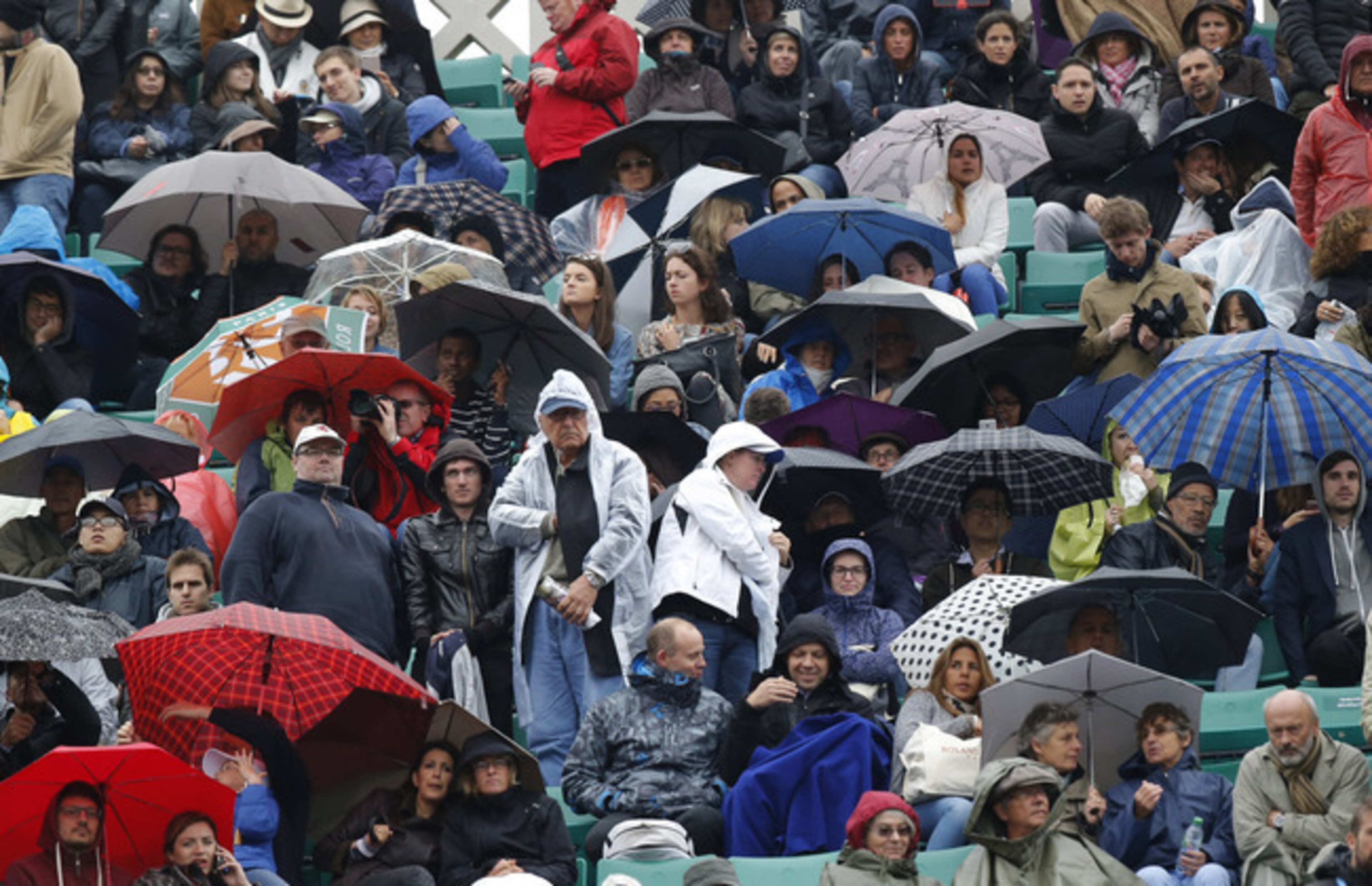 Fans cover up to endure rainy weather at Roland Garros at the 2016 French Open.