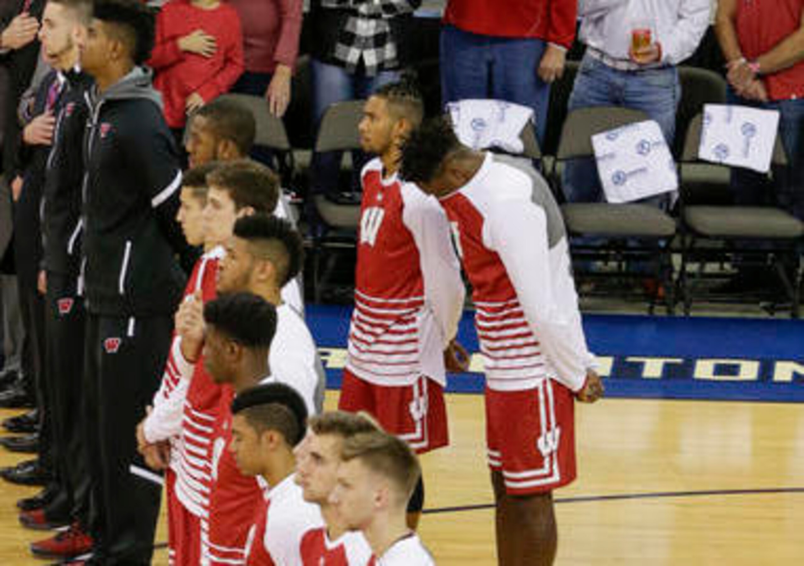 Jordan Hill (left) and Nigel Hayes stand behind teammates during the national anthem.